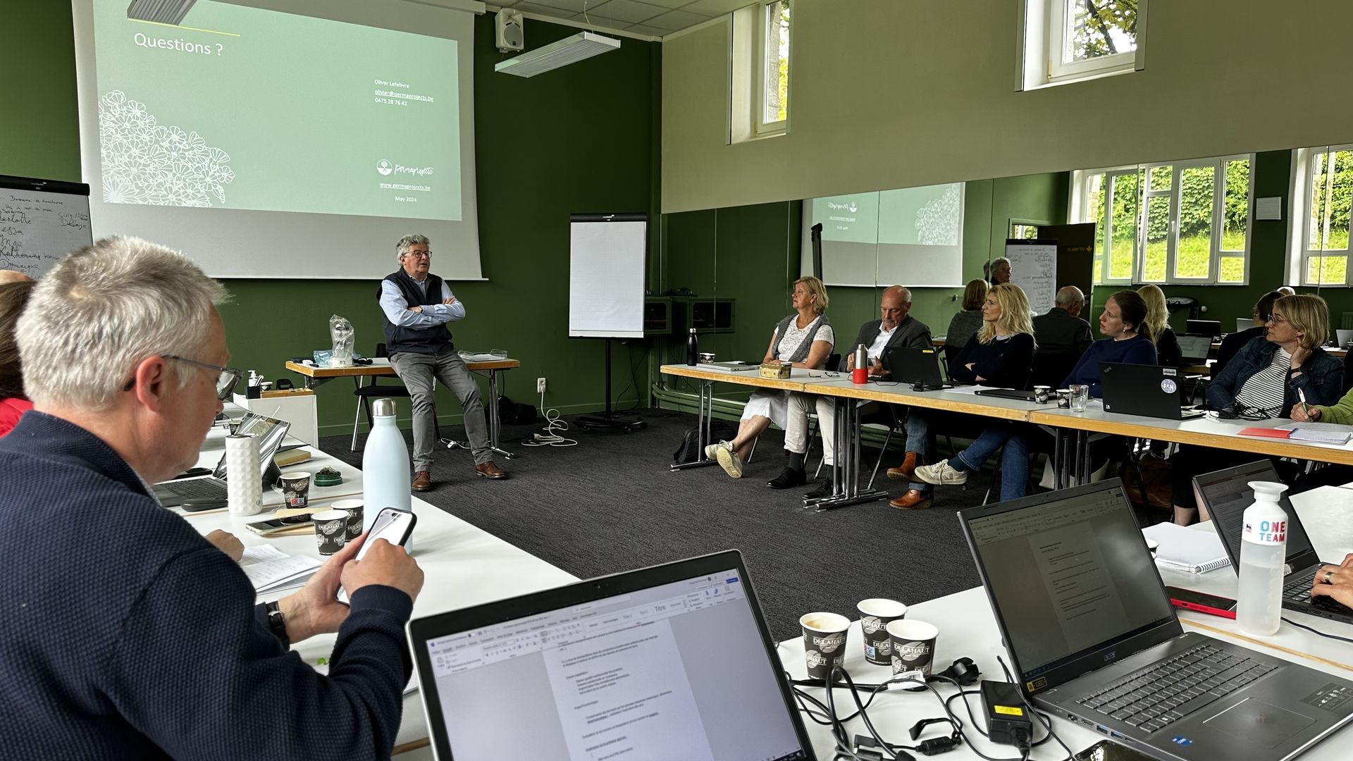 Groupe d'adultes autour de tables en U, écoutant un formateur s'exprimer